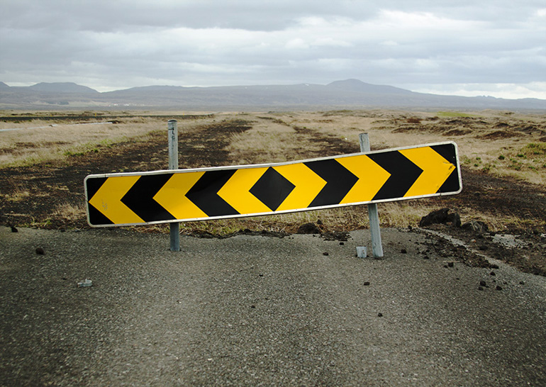 A yellow and black chevron road sign at the end of a road.