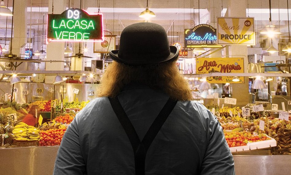 A person wearing a hat standing in front of a grocery produce section.