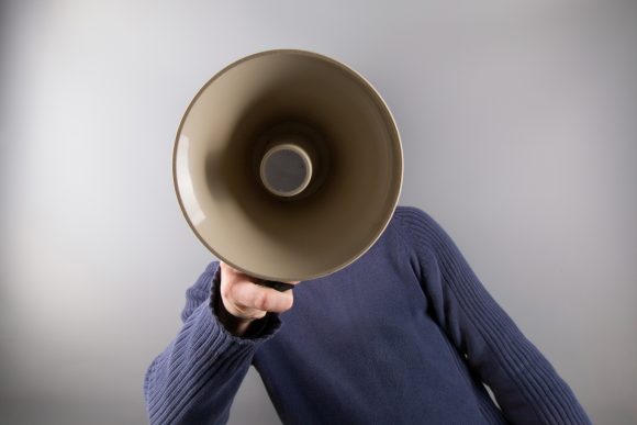 A person in a blue sweater holding a megaphone in front of their face.