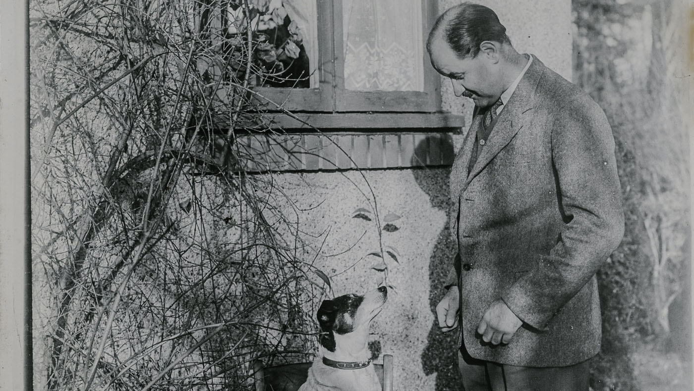 Old photograph of a man in a suit looking down at a dog.