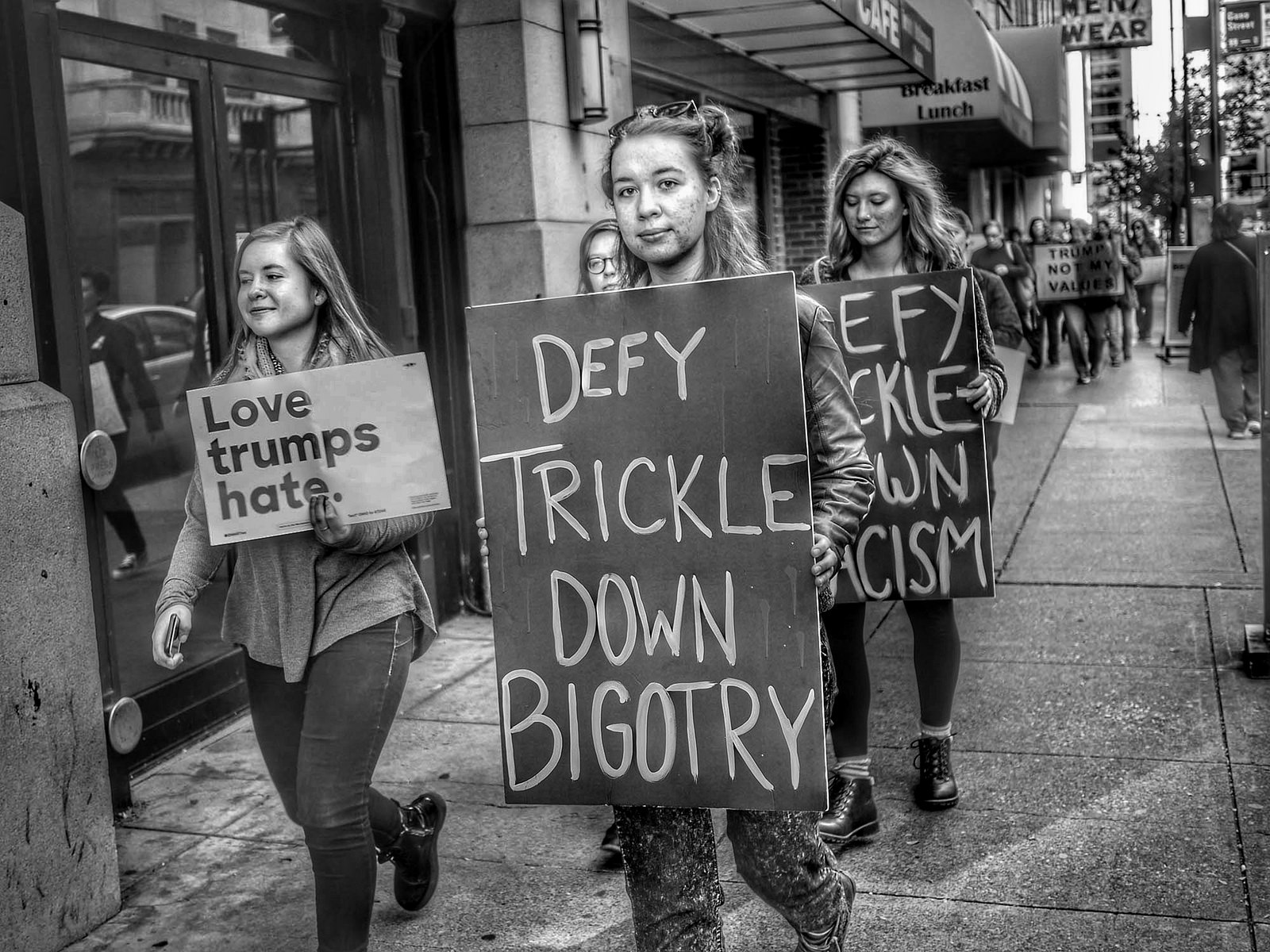 Women holding protest signs that read "Defy Trickle Down Bigotry," and "Love trumps hate."