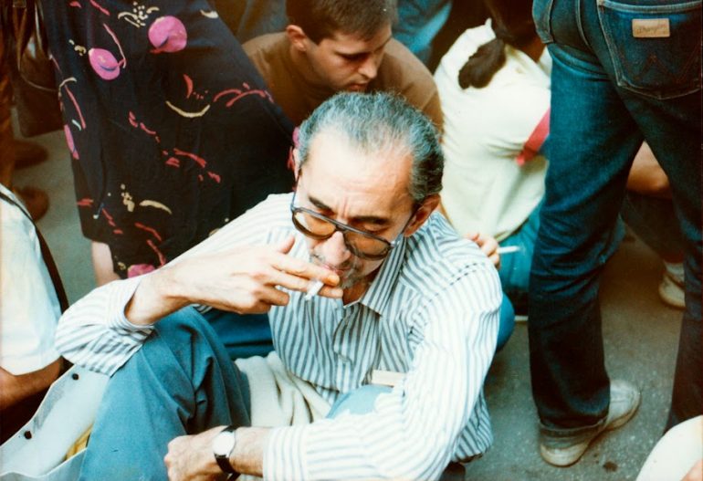 Old man sitting in a crowd and smoking a cigarette. 