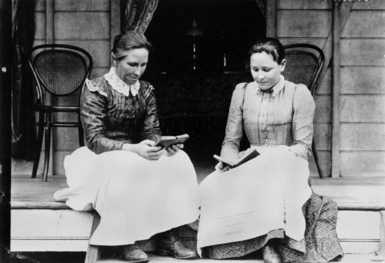 Old photo of two women reading from small books.