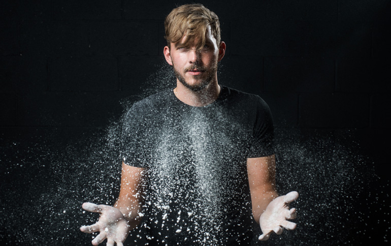 Man with outstretched hands and white particles lingering in front of him.