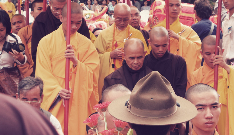 Men in yellow robes in a crowd holding red poles.