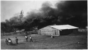 Black and white photo of people running from a burning barn.