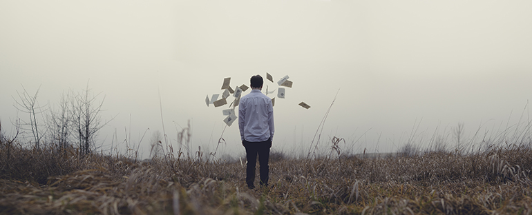 Man standing in a dry field with envelopes floating around him.