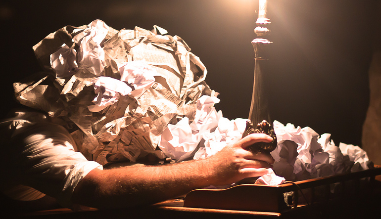 man buried under a pile of crumpled paper holds a lamp