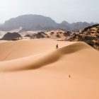 person walking up a vast sand dune