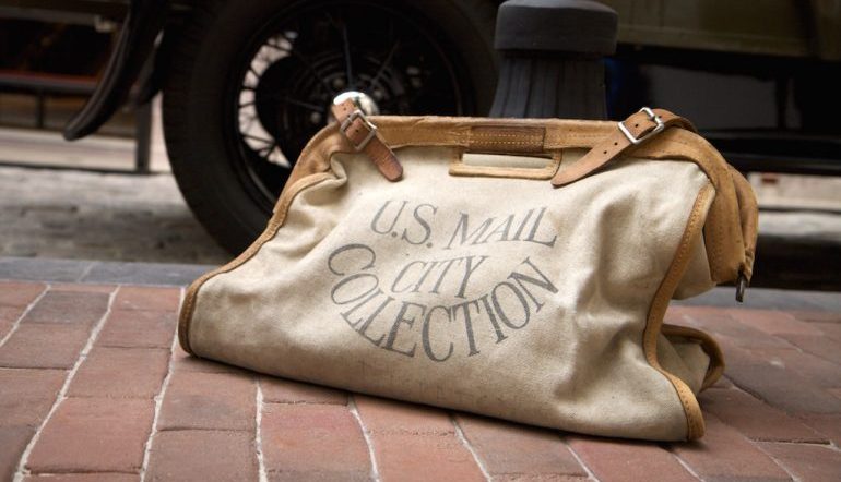 bag with lettering that reads "U.S. MAIL CITY COLLECTION" on a brick sidewalk