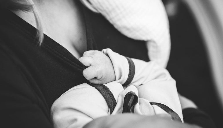 close up of baby's hands and head against mother's chest 