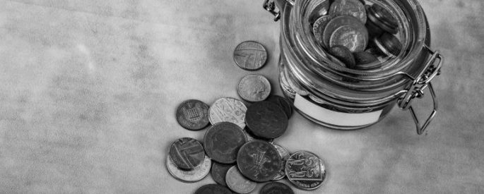 in black and white - glass tin of coins with coins scattered outside of it