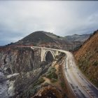 Photograph of a highway bridge going between two mountains over the ocean