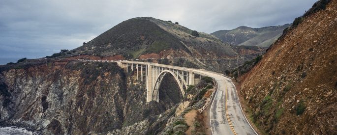 Photograph of a highway bridge going between two mountains over the ocean
