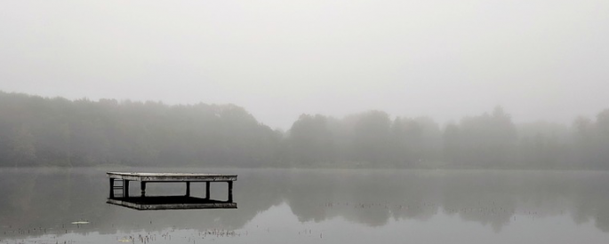 A lone dock sits in the middle of a grey, misty lake.