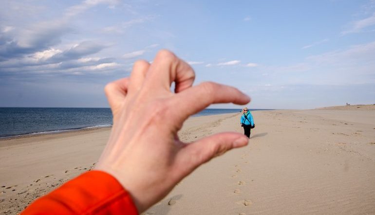 A photo of someone walking on a beach and the photographer's fingers seeming to crush the person walking