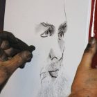 A hand sketching a charcoal portrait of a face