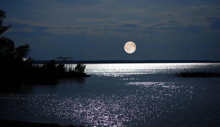 Photo of ocean bay with the moon low on horizon and lots of moonbeams on the water