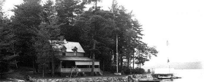 a black and white photograph of a house by a shallow river