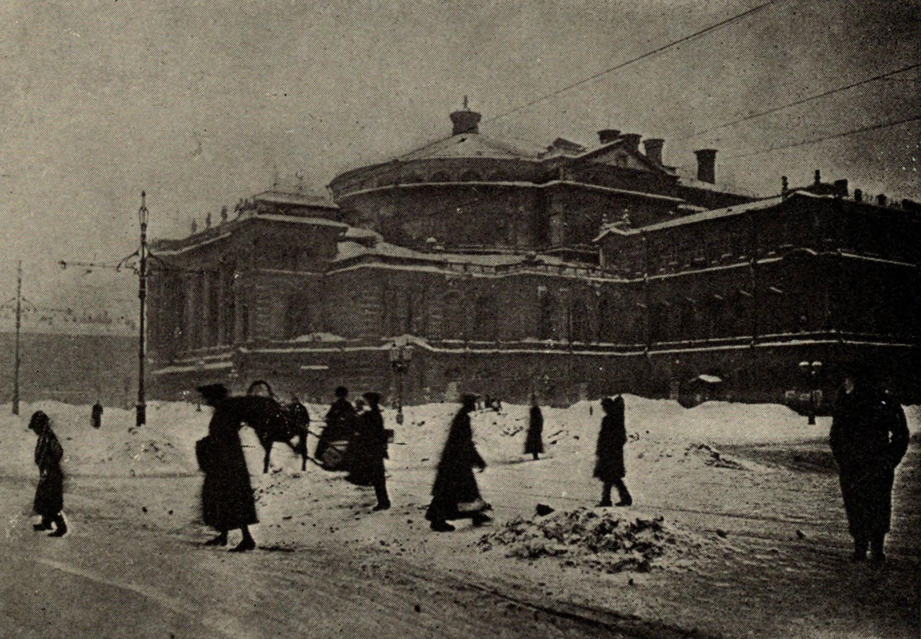 a black and white photograph of a Russian theatre in winter with people walking around