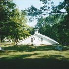 a photograph of a small white church in a wooded area