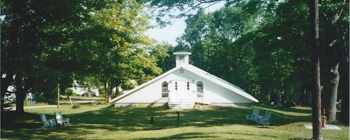 a photograph of a small white church in a wooded area
