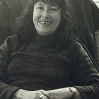 black and white image shows the poet Denise Levertov seated in an armchair and smiling