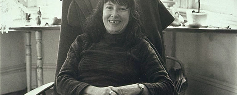 black and white image shows the poet Denise Levertov seated in an armchair and smiling 