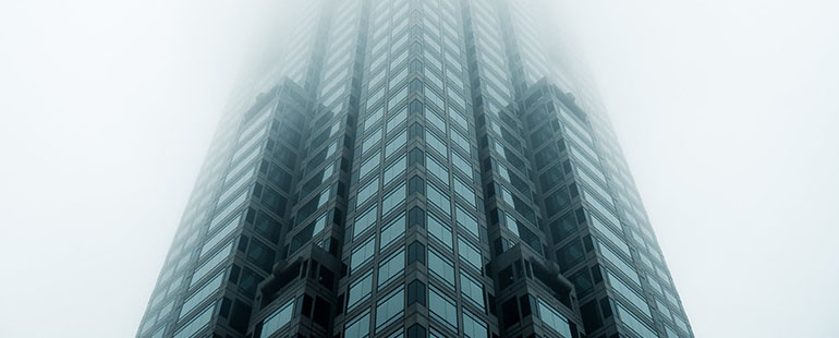 photograph of a high rise, glass building taken from below - the building stretches high up into a cloudy, foggy, gray sky, obscuring the top of the building