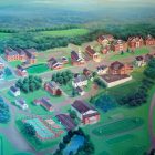 painting of the campus of Nichols College, with a myriad of brick buildings, a football field, and winding paths carved out from a surrounding, green forest