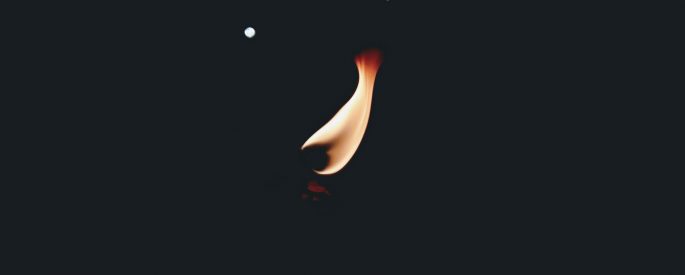 a small, orange flame stands out against a dark, almost pitch-black background
