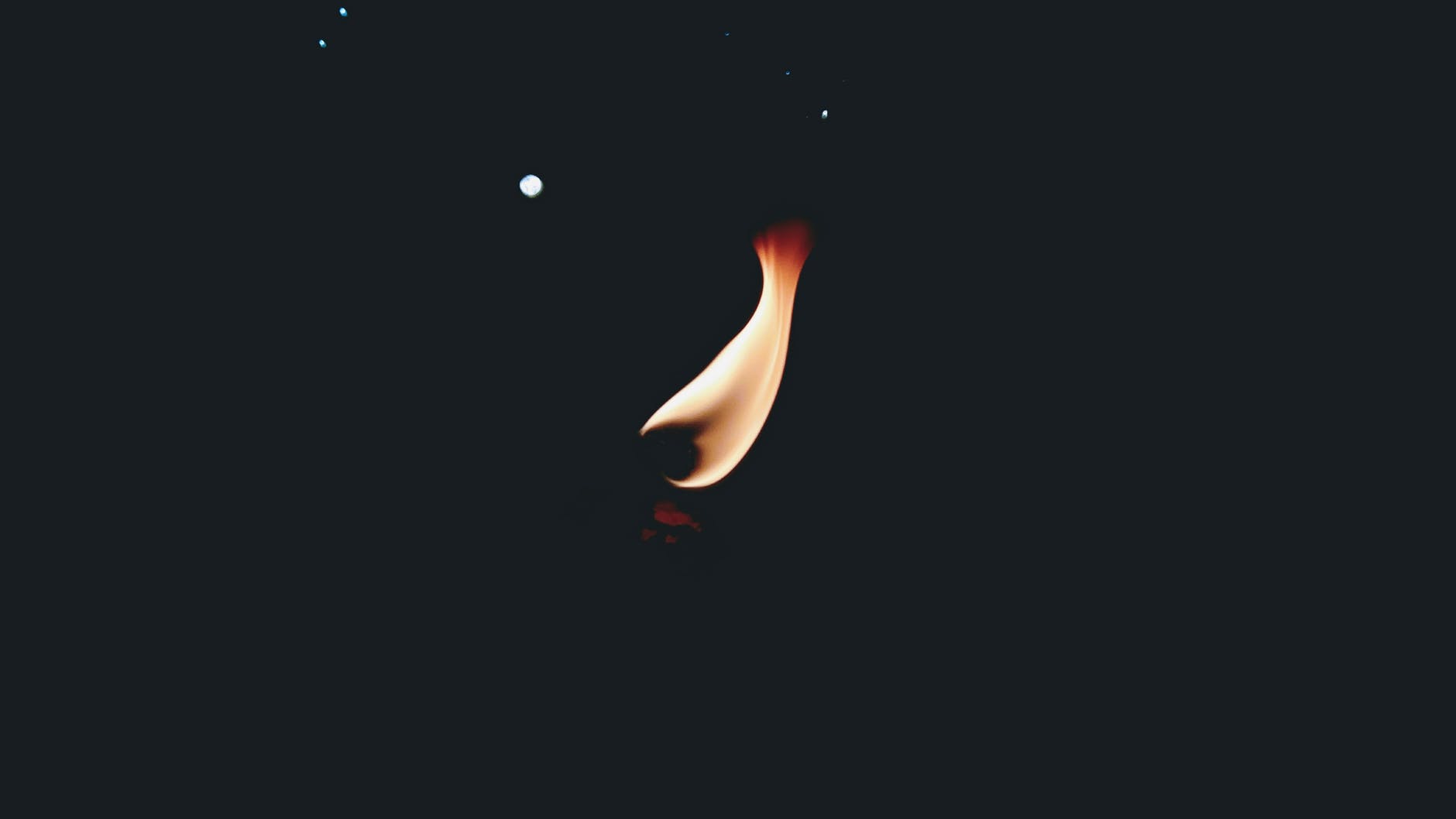 a small, orange flame stands out against a dark, almost pitch-black background 