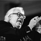 black and white photograph of Ray Bradbury, speaking at a microphone, with his hands gesturing upwards as he speaks