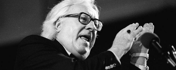 black and white photograph of Ray Bradbury, speaking at a microphone, with his hands gesturing upwards as he speaks