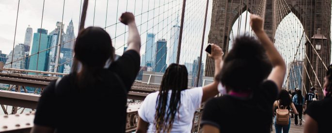photograph of Black activists from behind with their fists raised as they march across the Brooklyn Bridge