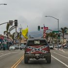 photograph of a pick up truck with a confederate flag on the tailgate. the truck is driving own a street--the background consists of an intersection and palm trees