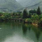 a photo taken by the author of this piece, image of a peaceful lake with two figures on a board in the middle of the lake--it is surrounded by mist colored mountains and lush landscapes