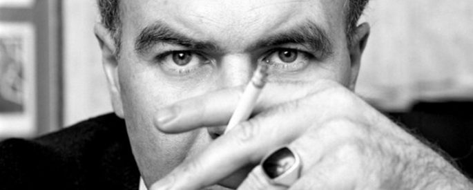 black and white photo of Raymond Carver holding a cigarette in front of his face and looking directly into the camera