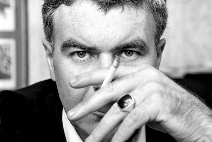 black and white photo of Raymond Carver holding a cigarette in front of his face and looking directly into the camera 