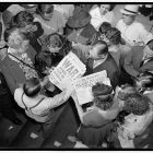 a black and white photograph of a crowd of people looking at a newspaper that says WAR