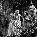a film still from the 1935 version of A Midsummer Night's Dream, featuring Helena and Hermia talking with each other while Puck watches on