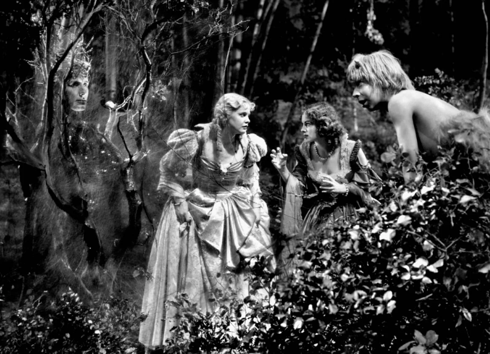a film still from the 1935 version of A Midsummer Night's Dream, featuring Helena and Hermia talking with each other while Puck watches on