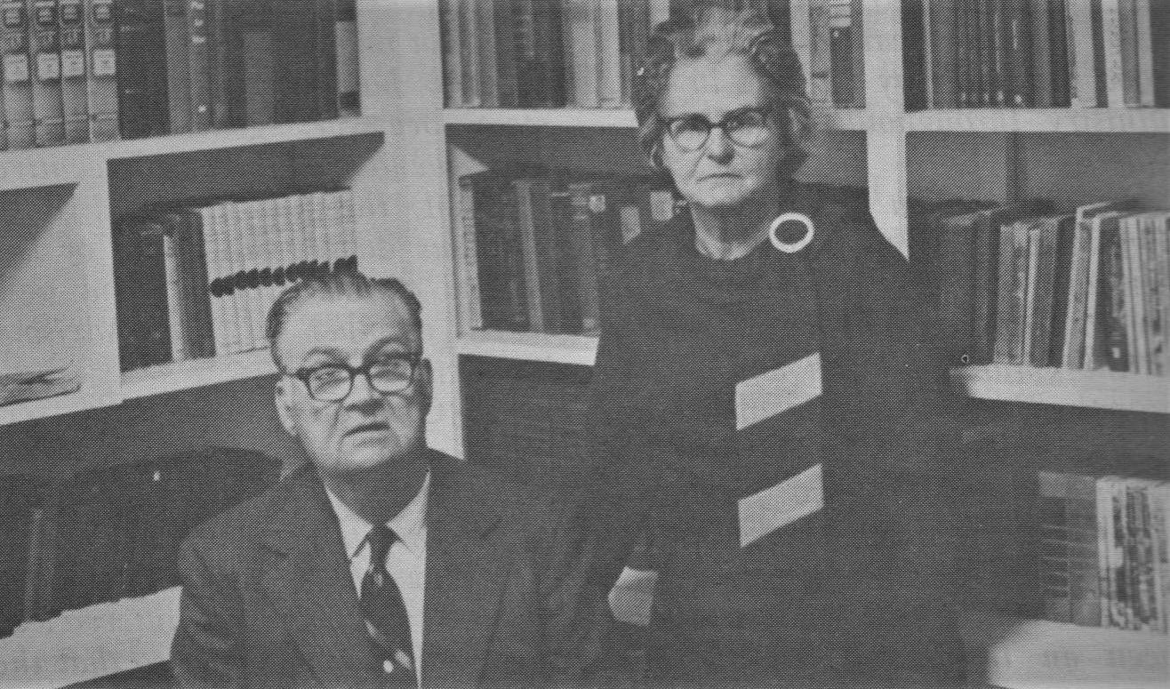 a black and white photograph of an older man and woman in front of a bookshelf